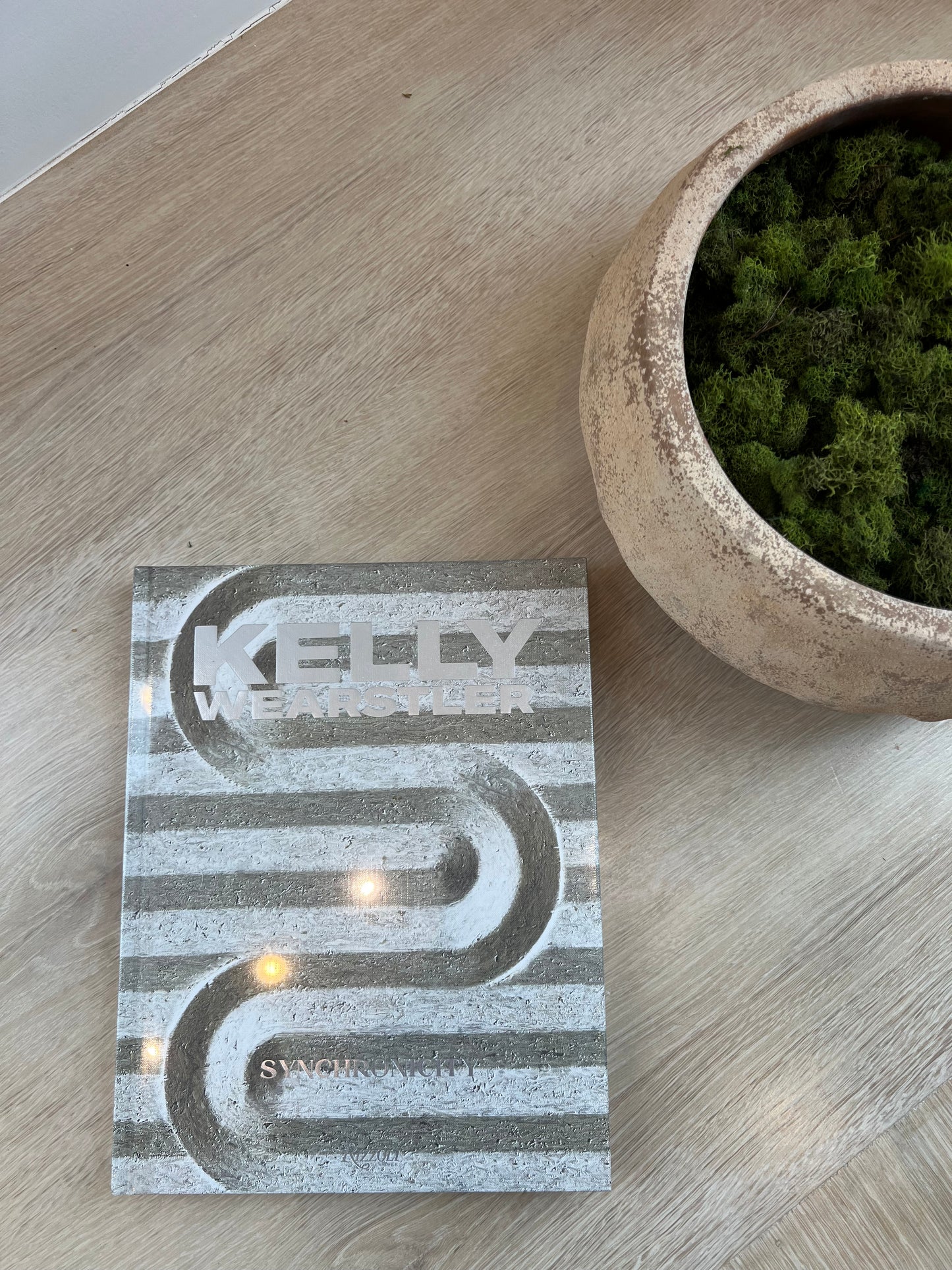 Decorative book with geometric design on a wooden surface next to a pot of moss.