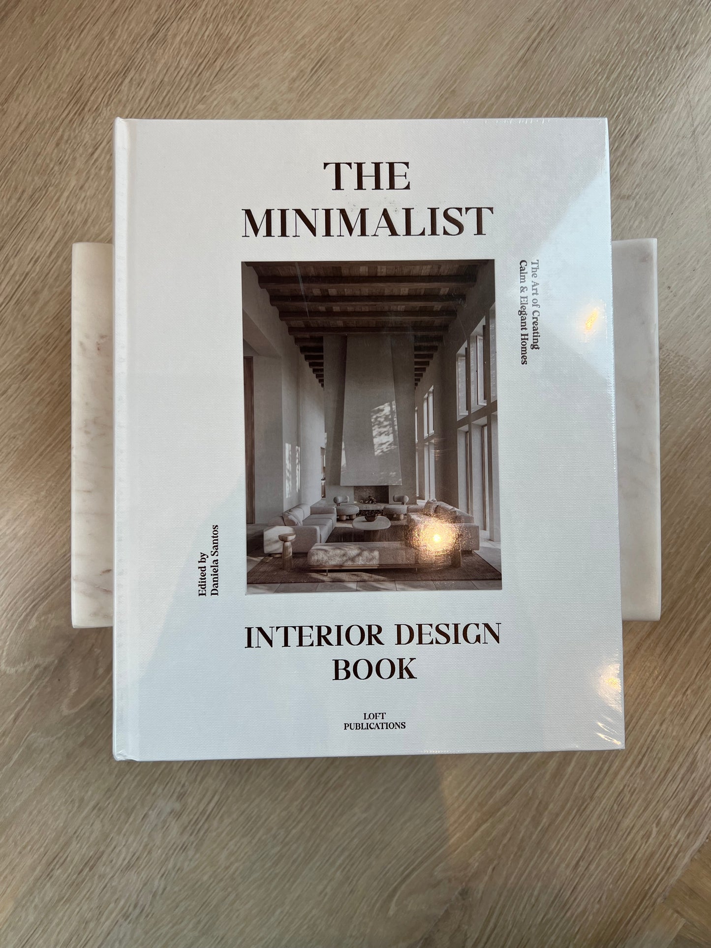 Book titled 'The Minimalist Interior Design Book' on a wooden surface