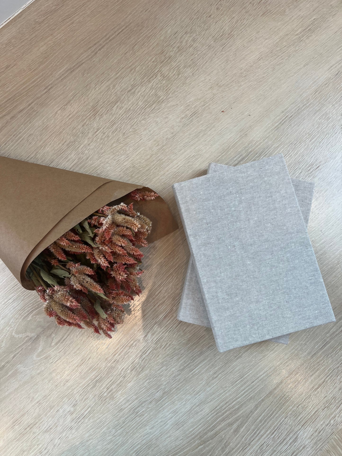 Bouquet of dried flowers in a brown paper bag on a light wooden floor with two gray envelopes.