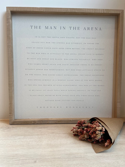 Framed text art with a decorative bouquet of dried flowers on a light wooden surface.