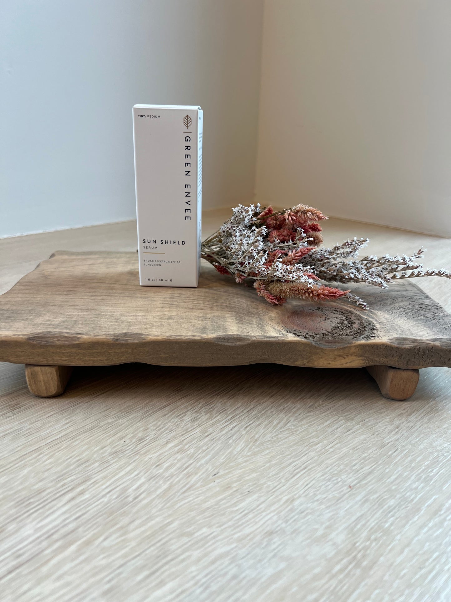 Wooden surface with dried flowers and a 'Green Envy' product card on a light background