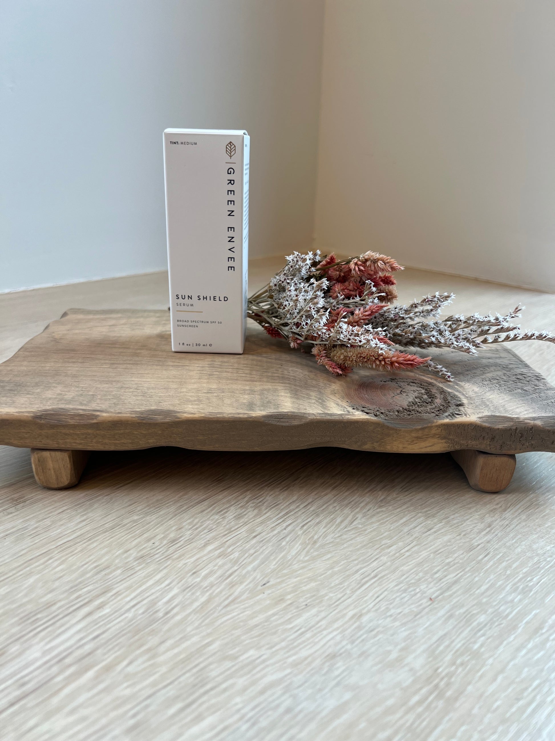 Wooden surface with dried flowers and a 'Green Envy' product card on a light background