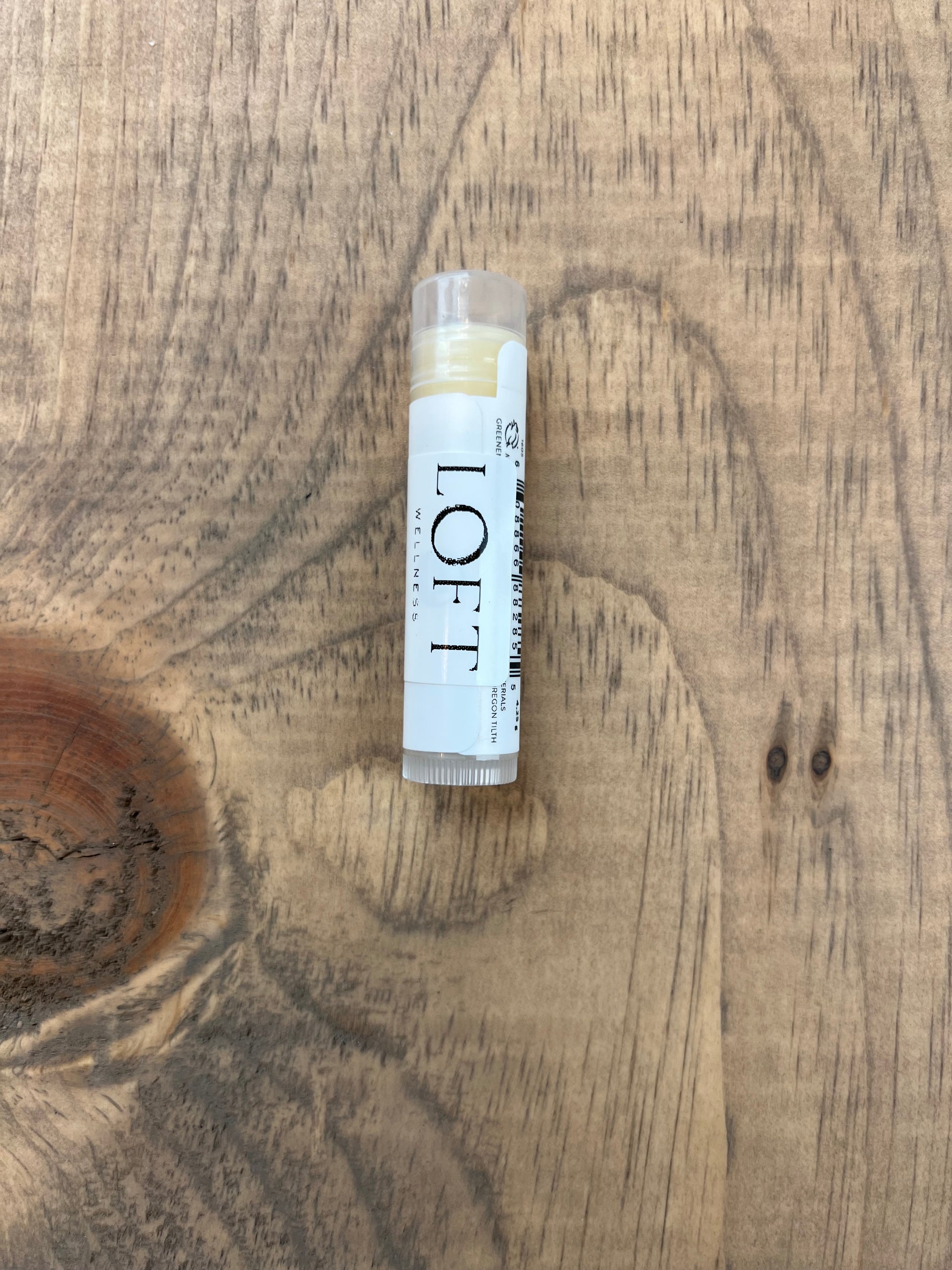 Lip balm stick labeled 'LOFT' on a wooden surface