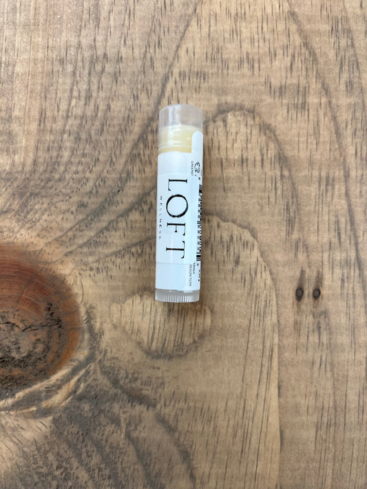 Lip balm stick labeled 'LOFT' on a wooden surface