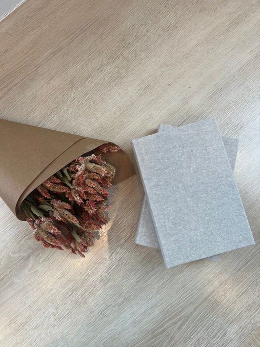 Bouquet of dried flowers in a brown paper bag on a light wooden floor with two gray envelopes.
