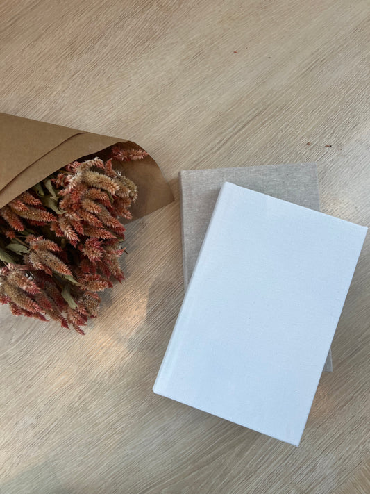 White box on a wooden surface with a bouquet of dried flowers in a brown paper bag.